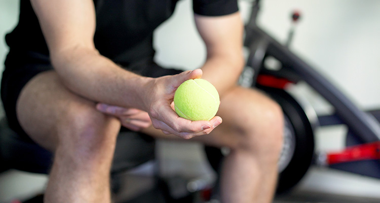 Jon Crim Holding a Tennis Ball While Demonstrating Wrist Exercises